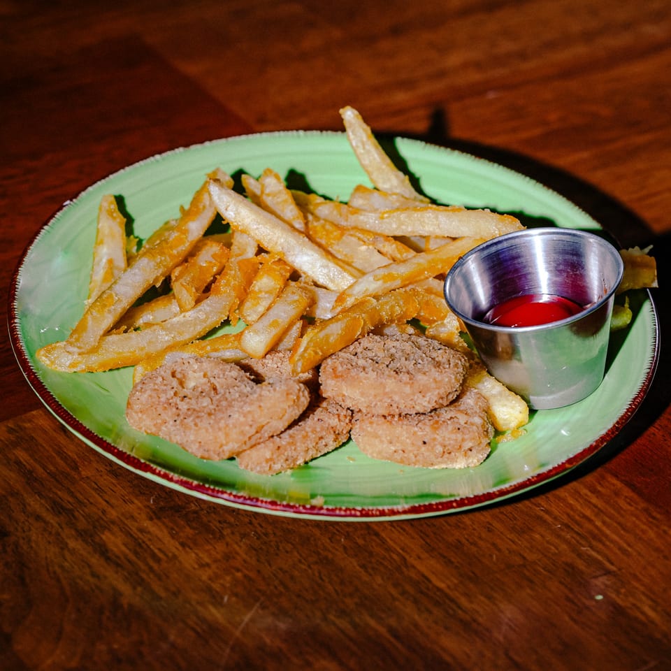 Crispy french fries and chicken nuggets with a side of ketchup on a green plate.