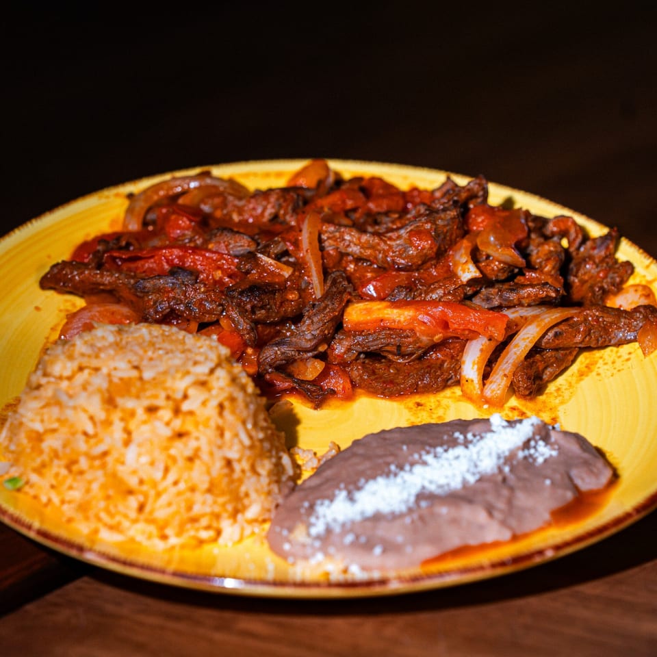 Whiskylucan Miami's Mexican fajitas with rice and refried beans on a yellow plate.