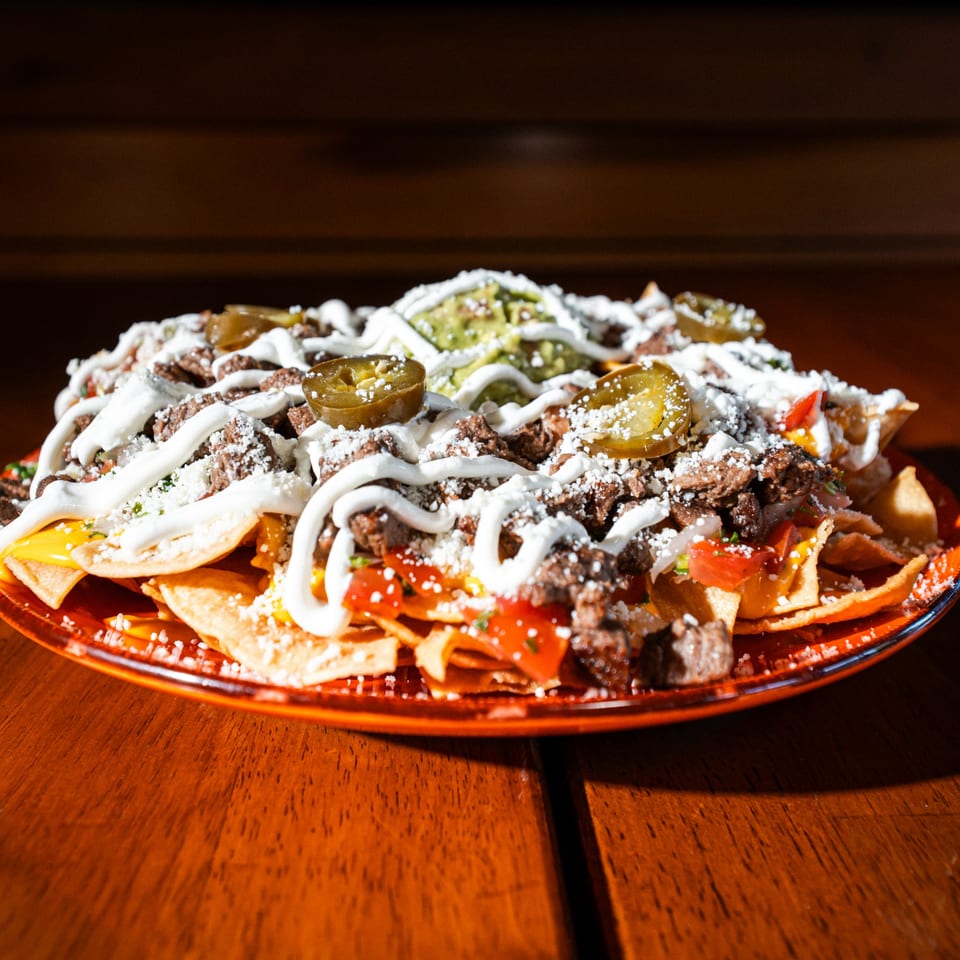 Whiskylucan Miami's carne asada nachos with cheese, sour cream, guacamole, and jalapeños on a red plate.