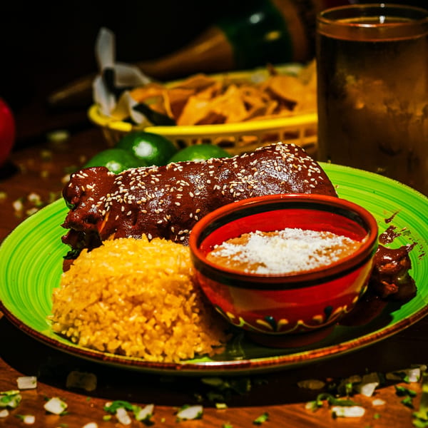 Mexican mole ribs with rice and beans on a green plate, with limes and chips in the background.