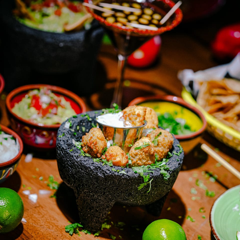 Fried Mexican appetizers with dipping sauce in a molcajete, surrounded by guacamole and limes.