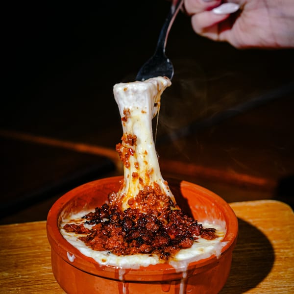 A fork lifts a string of melted cheese from a bubbling Mexican queso fundido with chorizo.
