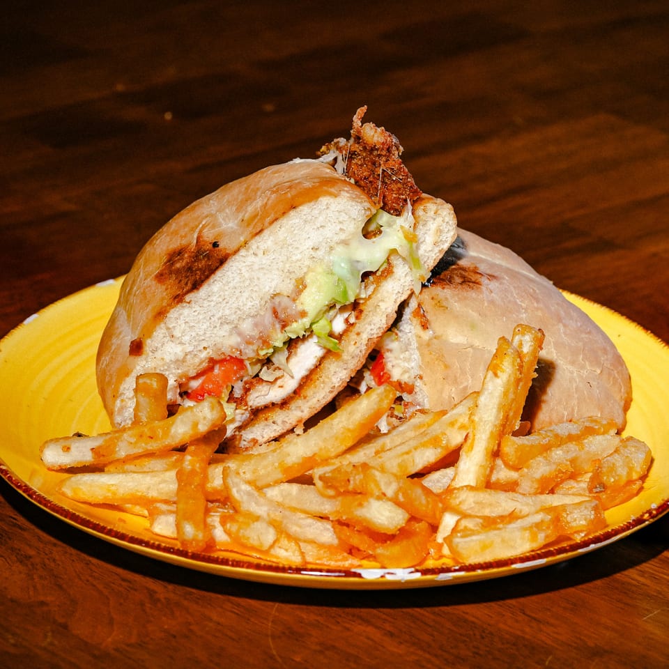 A Mexican torta sandwich with chicken, avocado, and lettuce, served with a side of fries.