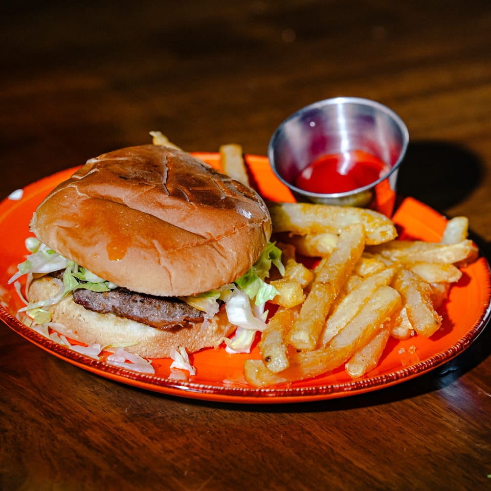 A burger with lettuce and a side of golden fries and ketchup on an orange plate.