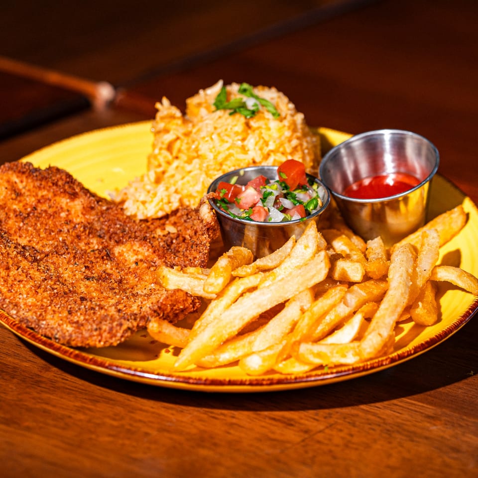 Breaded chicken, Mexican rice, french fries, pico de gallo, and ketchup on a yellow plate.