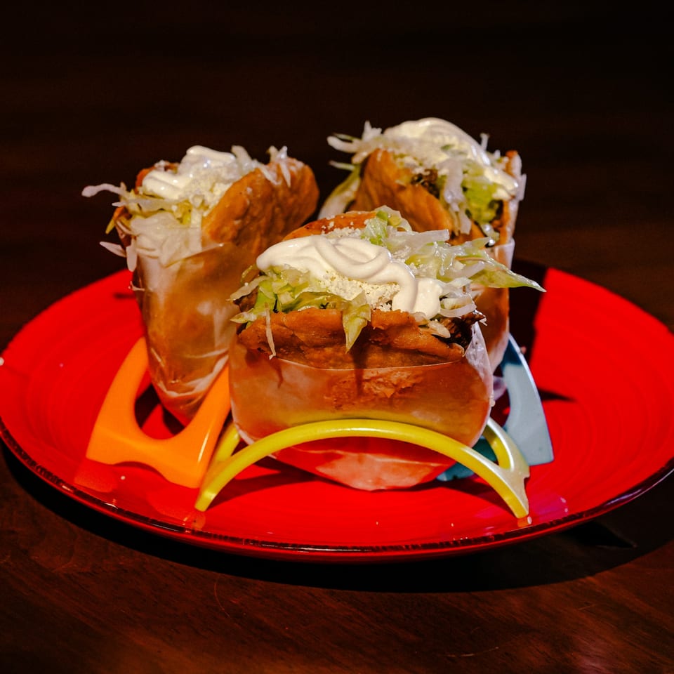Three crispy Mexican tacos with shredded lettuce, cheese, and sour cream on a red plate.
