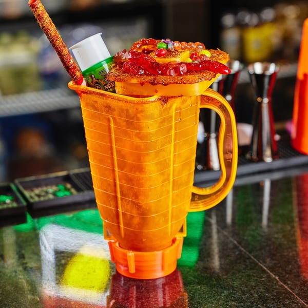 A vibrant orange Mexican michelada, topped with candies, gummies, and a chili-dusted straw.