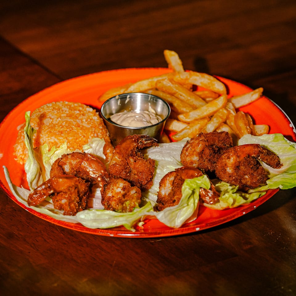 Whiskylucan Miami's fried shrimp with rice, french fries, and dipping sauce on an orange plate.