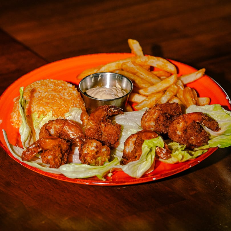 Whiskylucan Miami's fried shrimp with rice, french fries, and dipping sauce on an orange plate.