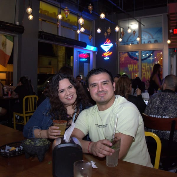 Smiling couple enjoying drinks and guacamole at a lively Mexican restaurant with neon signs.