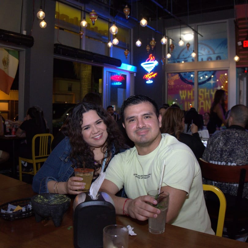 Smiling couple enjoying drinks and guacamole at a lively Mexican restaurant with neon signs.