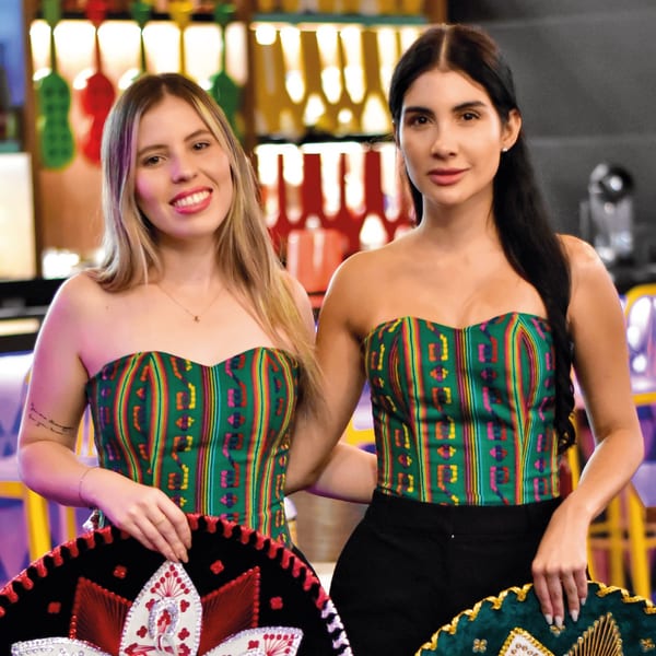 Two women in colorful Mexican-inspired tops hold sombreros in a vibrant restaurant setting.
