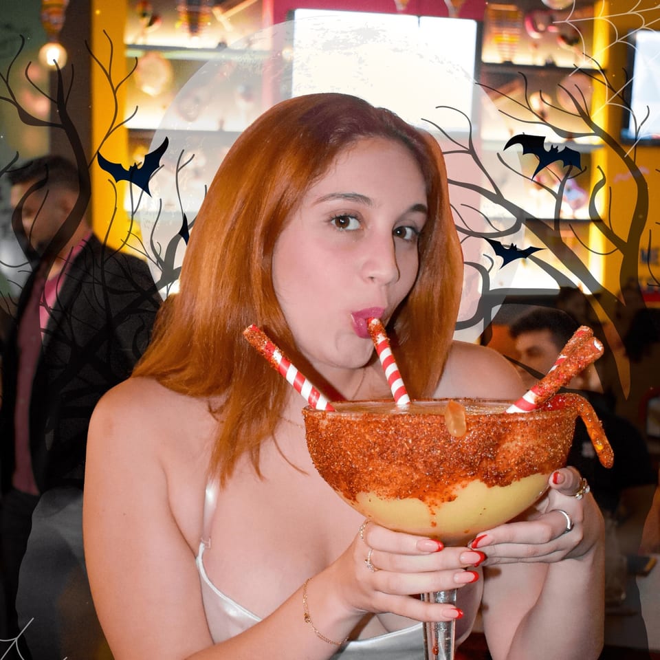 Woman with red hair sips a large, chili-rimmed margarita with Halloween-themed overlays.