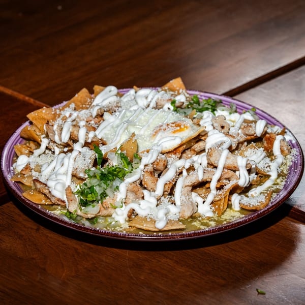 A plate of Mexican chilaquiles with chicken, green sauce, sour cream, cheese, and a fried egg.